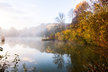 Naklejka na ściany i meble Beautiful landscape with lake and forest. Amazing nature wallpaper. Autumn trees in foggy morning. Romantic place. 