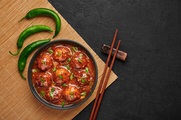 Veg Manchurian Gravy Balls in black bowl in dark slate table top. Vegetarian Manchurian is indian chinese cuisine dish. Asian food and meal. Top view. Copy space