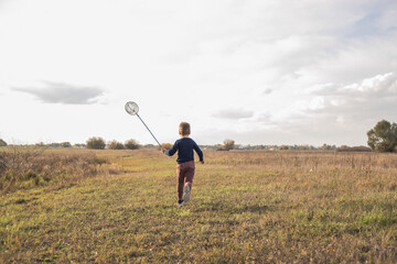 Young boy with butterfly net walking meadow. Child playing catching insects. Seasonal summer activity for kids outdoor. Learning animal fauna world hobby. View from back.