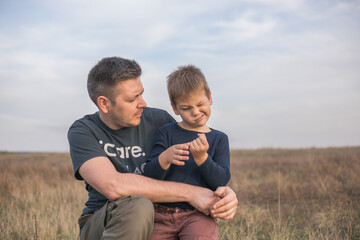 Naklejka na ściany i meble Happy dad hugging son on the meadow background. Concept of father-son relationship