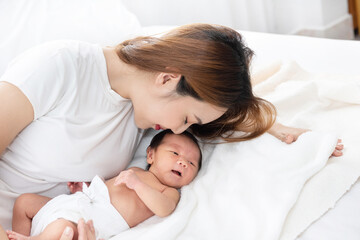 Obraz na płótnie Canvas Beautiful asian women mother long hair in the white pajamas. mom kiss at newborn infant with love, while a baby sleeping in her arm with warm, safe, comforted resting on the clean bed.
