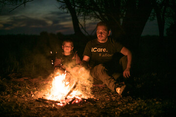 Father and little cute son sitting by the fire in the forest. Best friends spending time together.