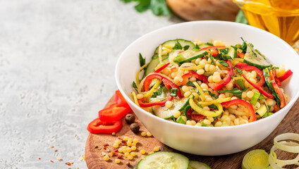 Vegetable salad with ptitim in a white bowl on a gray background. Copy space for text. Salad made...