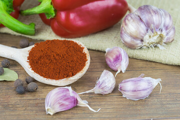 Natural, organic red pepper on wooden background with 
spice on a spoon and a bunch of garlic