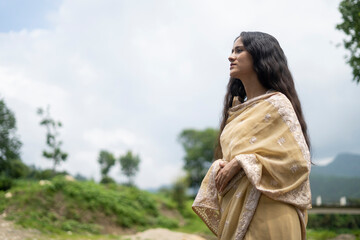 Beautiful Indian young female model wearing traditional saree standing in front of a river...