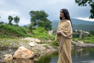 Beautiful Indian young female model wearing traditional saree standing in front of a river...