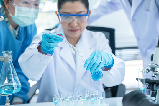 Scientist woman with team working with liquids in glassware. Asian scientist works in modern biological lab. Female clinician working with liquids in laboratory. 