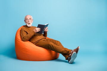 Portrait of his he nice attractive amazed stunned bearded grey-haired man sitting in bag chair reading book pout lips reaction new information isolated over blue pastel color background