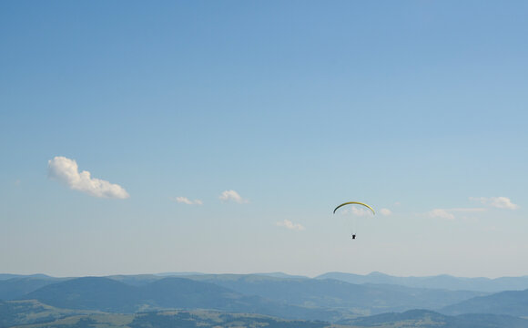 Paraglider flying over Carpathian mountains against clear sky in summer day
