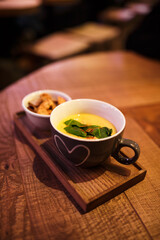 Serving cream soup in a cup with a cup of rusks on a wooden tray