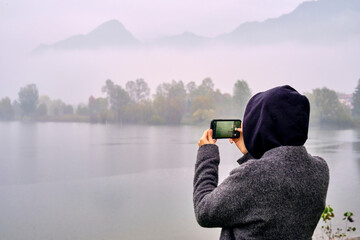A person photographing a foggy lake on a cold day