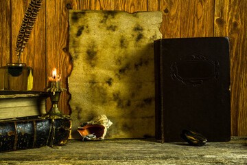 A sheet of yellowed paper with space for text, an inkwell with a feather, old books and documents in scrolls, a burning candle on a wooden background.