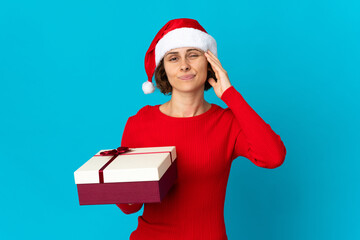 English girl with christmas hat holding a present isolated on blue background having doubts