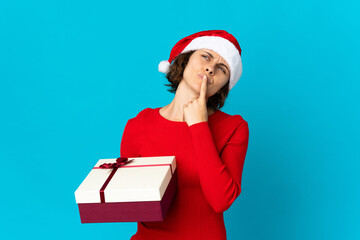 English girl with christmas hat holding a present isolated on blue background having doubts while...