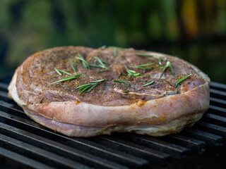 a large piece of pork leg with rosemary on the bone is fried on the grill. cooking on the grill.