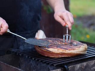 Fototapeta premium a man roasts a large steak on the grill. steak with a pork leg bone.