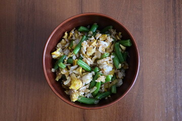 Top view of the fried rice with egg and green beans in the brown ceramic bowl on a wooden table close-up. Top view. Selective focus