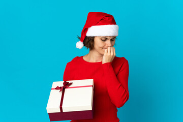 English girl with christmas hat holding a present isolated on blue background having doubts
