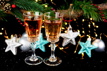 New Year and Christmas decor. Glasses for champagne, toys for the Christmas tree stand on the table in front in the dark, beautiful bokeh on the background. Close-up.