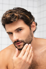 Shirtless man touching chin while looking at camera in bathroom