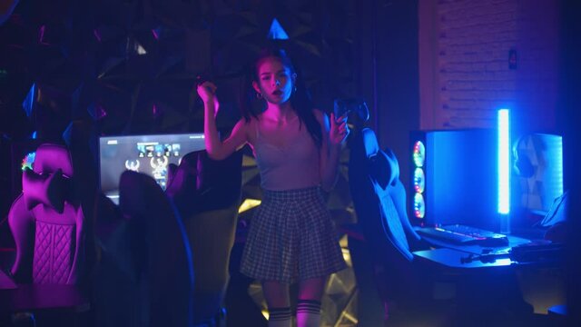 Young sexy daring woman with ponytail holding a joystick in neon gaming club and blows a bubble gum 
