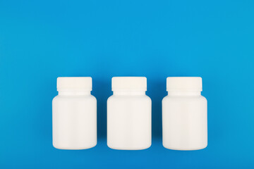 Three white plastic bottle with medicine on blue background with space for text