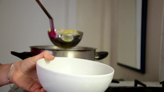 Girl puts chicken broth or soup in a bowl with a ladle. The cooks chicken soup. Puts chicken in a pan, pours water.
