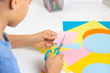 Kid hands cutting colored paper with scissors. Education, learning, paper craft, entertainment at home