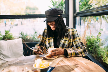 Young tourist fashionable black woman with a smile sitting on a cafe terrace holding a cup of...