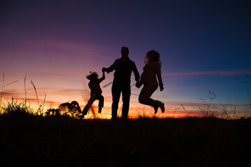 Fototapeta na wymiar Silhouette of a Happy family jumping on sunset 