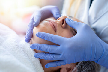 Cosmetologist hands in blue gloves touch face of young patient making massage