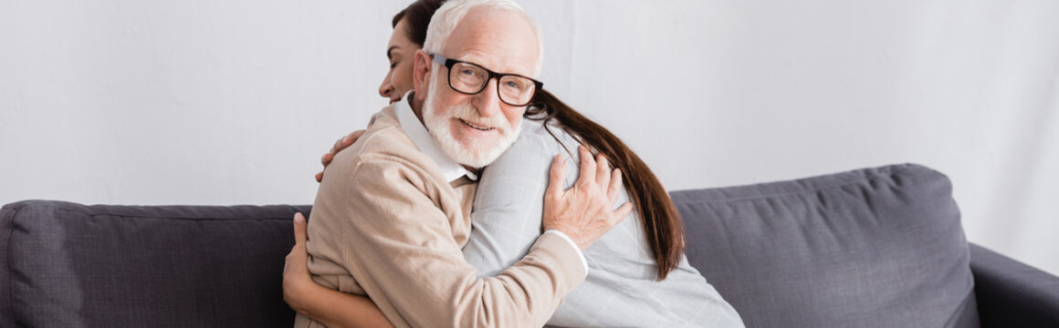 Elderly Man Smiling At Camera While Hugging Adult Daughter At Home, Banner