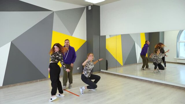 Trio of young dancers dancing hip hop in a dance studio in front of the wall with bright geometric pattern