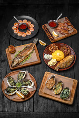 Fish and seafood dishes: oysters, trout, squid, shrimp. Several dishes on a background of black boards. Festive table with delicious food.