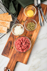 Gourmet Rindertatar Beef Tatar  aus Rindfleisch Filet fettarm  und roh, Kapern, Eigelb, Zwiebeln, Toast Brot auf Holzbrett und Marmor Hintergrund hell