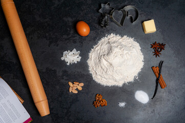 Several Ingredients for Cookies displayed in a circle on a slate plate. A pile of flour in the center. A rolling pin and aBook with recipes are on the side. Top shot.