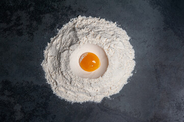 Preparation for a Cookie dough. A pile of flour with an egg in the middle on a slate plate.