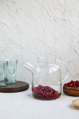 Cranberry juice in a glass transparent teapot on a concrete background. Berry cold drink. Making homemade lemonade.