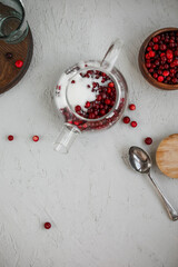 Cranberry juice in a glass transparent teapot on a concrete background. Berry cold drink. Making homemade lemonade.