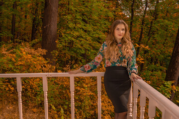 Joyful teenager stands leaning against a white railing young smiling at the camera blonde, in a colored shirt stands against a lake background innocent autumn professional real people bright blue eyes