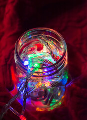 Lights inside the glass jar on a red sweater, colorful light glowing in the dark inside the jar.