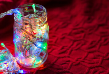 Lights inside the glass jar on a red sweater, colorful light glowing in the dark inside the jar.