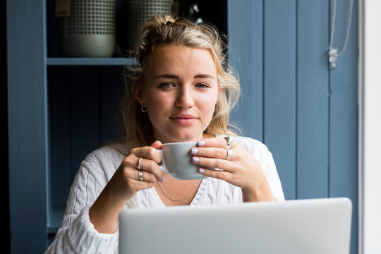 Young blond woman sitting alone at a cafe table with a cup of coffee