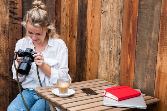 Young blond woman sitting alone at a cafe table, looking at digital camera display.