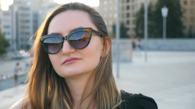 Portrait of young businesswoman in sunglasses walking in city street. Attractive business woman looking at the camera. Face of confident girl commuting to work. Close up Slow motion