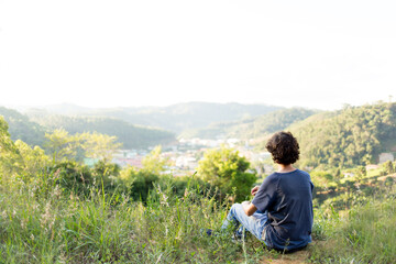 Young man sitting on the top of a mountain and watching the city in the valley on a sunny day.