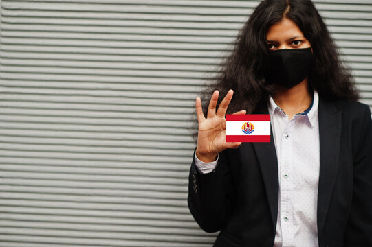 Asian woman at formal wear and black protect face mask hold French Polynesia flag at hand against gray background. Coronavirus at country concept.
