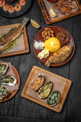 Fish and seafood dishes: oysters, trout, squid, shrimp. Several dishes on a background of black boards. Festive table with delicious food.