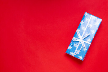 Fototapeta na wymiar mock up of a blue gift box with a white ribbon on a red background with space for text.