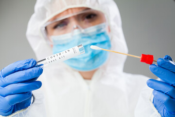 Medical healthcare technologist holding COVID-19 swab collection kit, wearing white PPE protective...